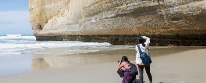 Deux personnes sur une plage photographiant la mer à Tunnel Beach en Nouvelle-Zélande